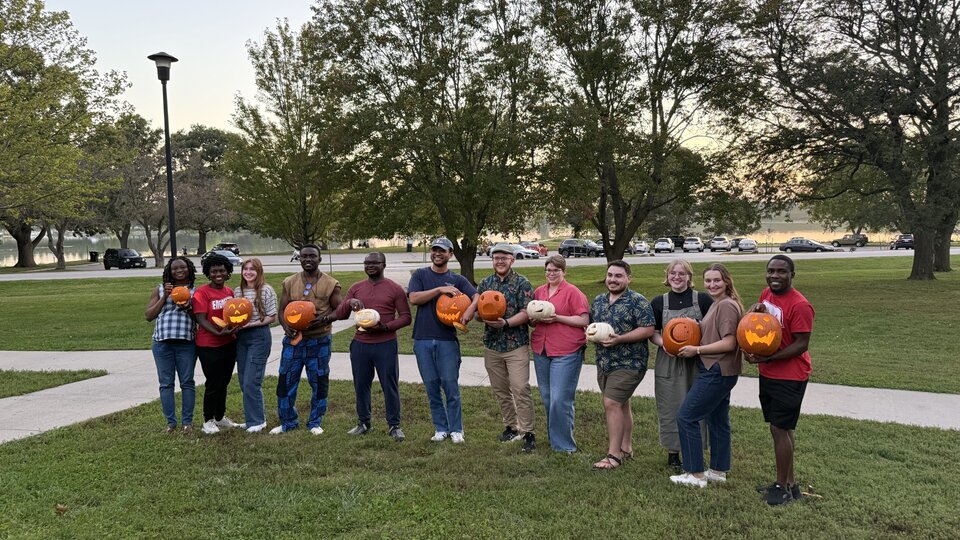 DBER Students and Community Members hold their freshly carved pumpkins during a fall picnic